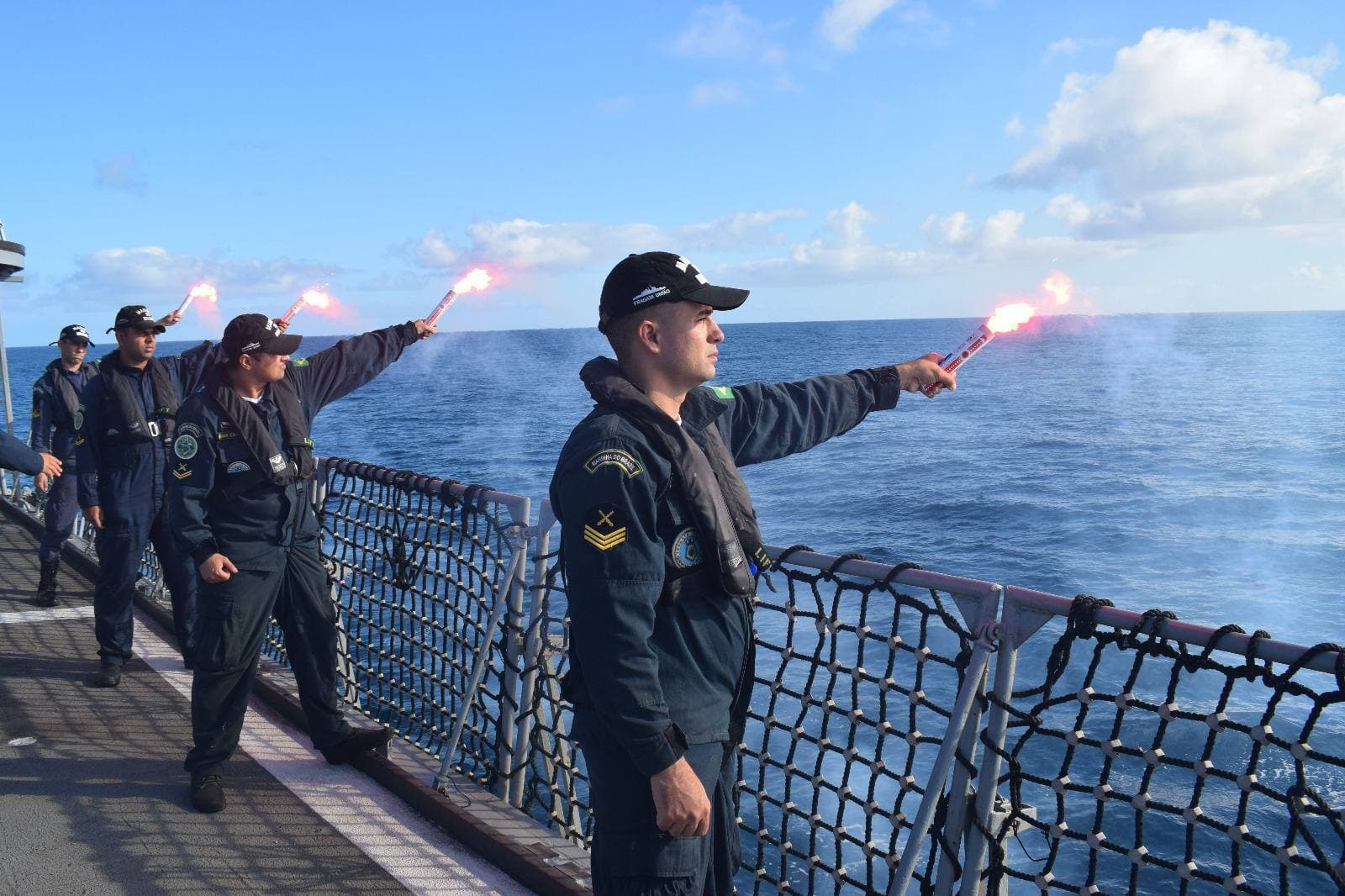 Tripulantes a acender fachos de mão vermelhos no convés de um navio