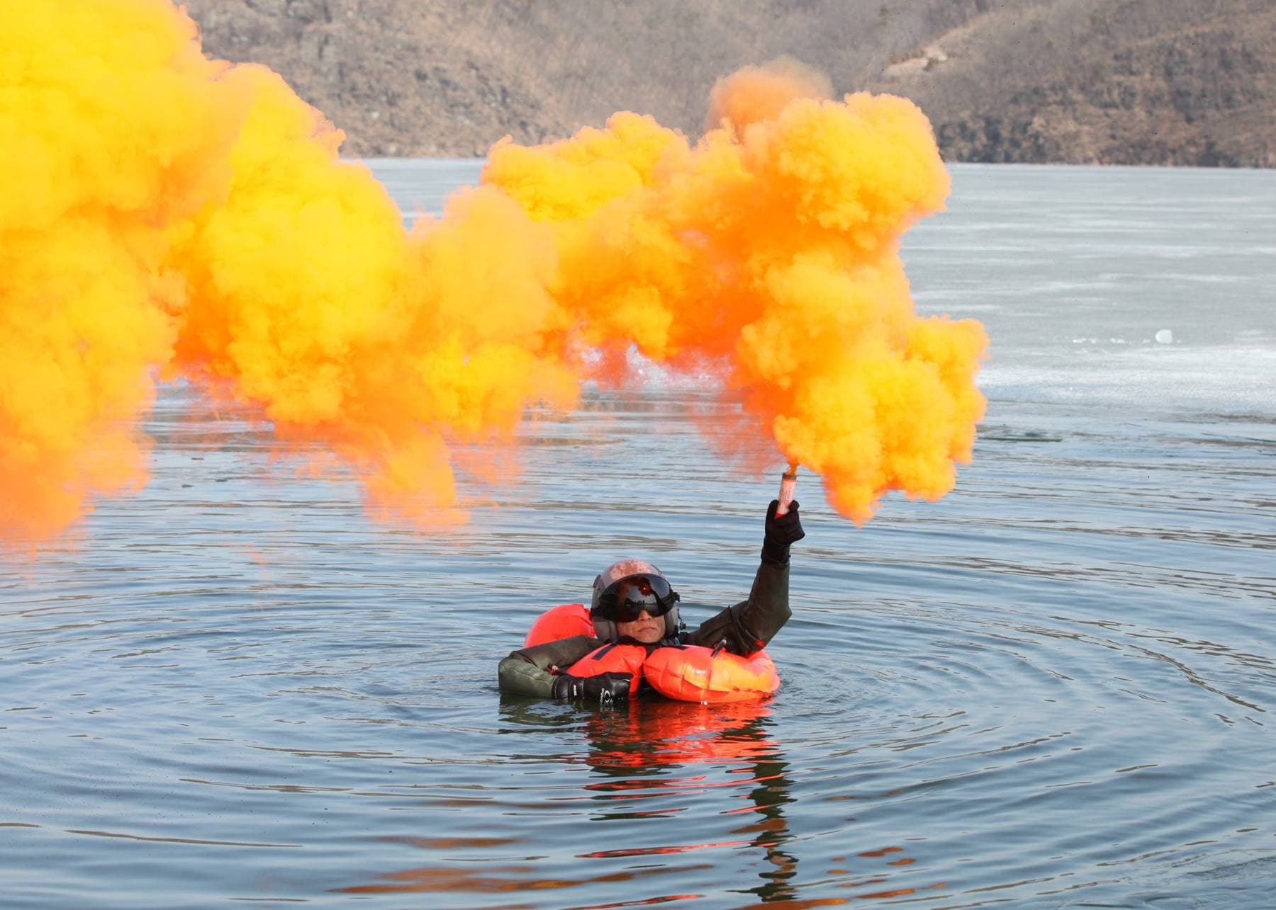Pessoa na água com colete salva-vidas a acender um sinal de fumo laranja